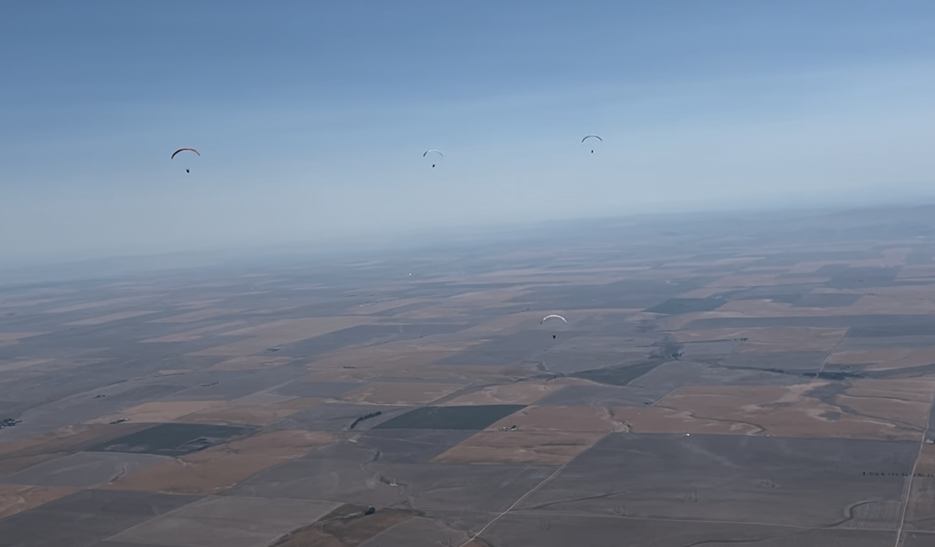 Five paragliders spot high above farmland with blue sky.