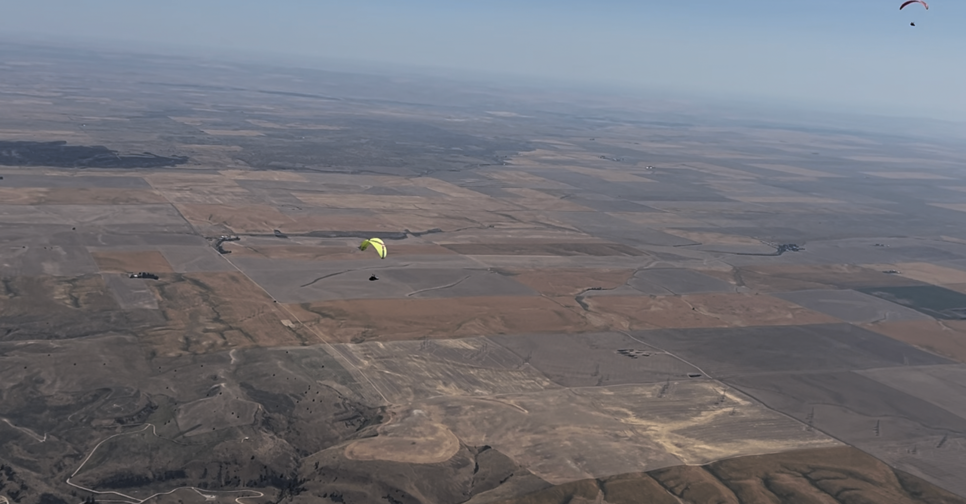 Paraglider flying solo over brown fields.