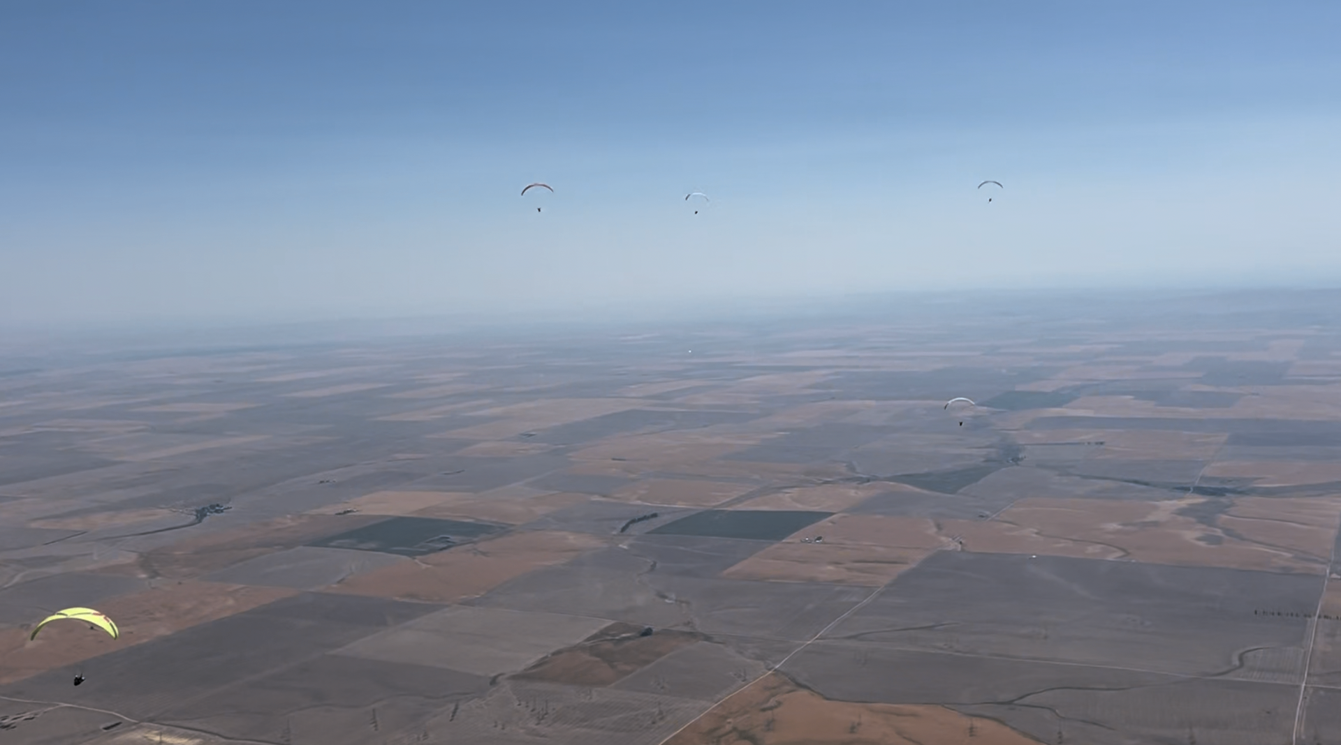 Wide view of five paragliders above a broad landscape.
