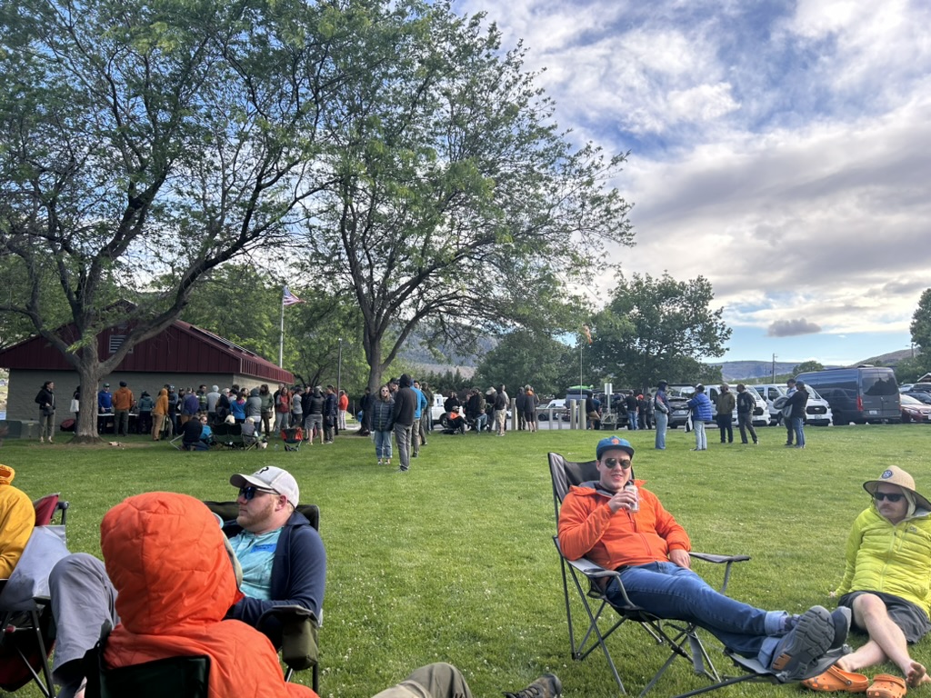 People relaxing and chatting in a grassy park during a paragliding event.