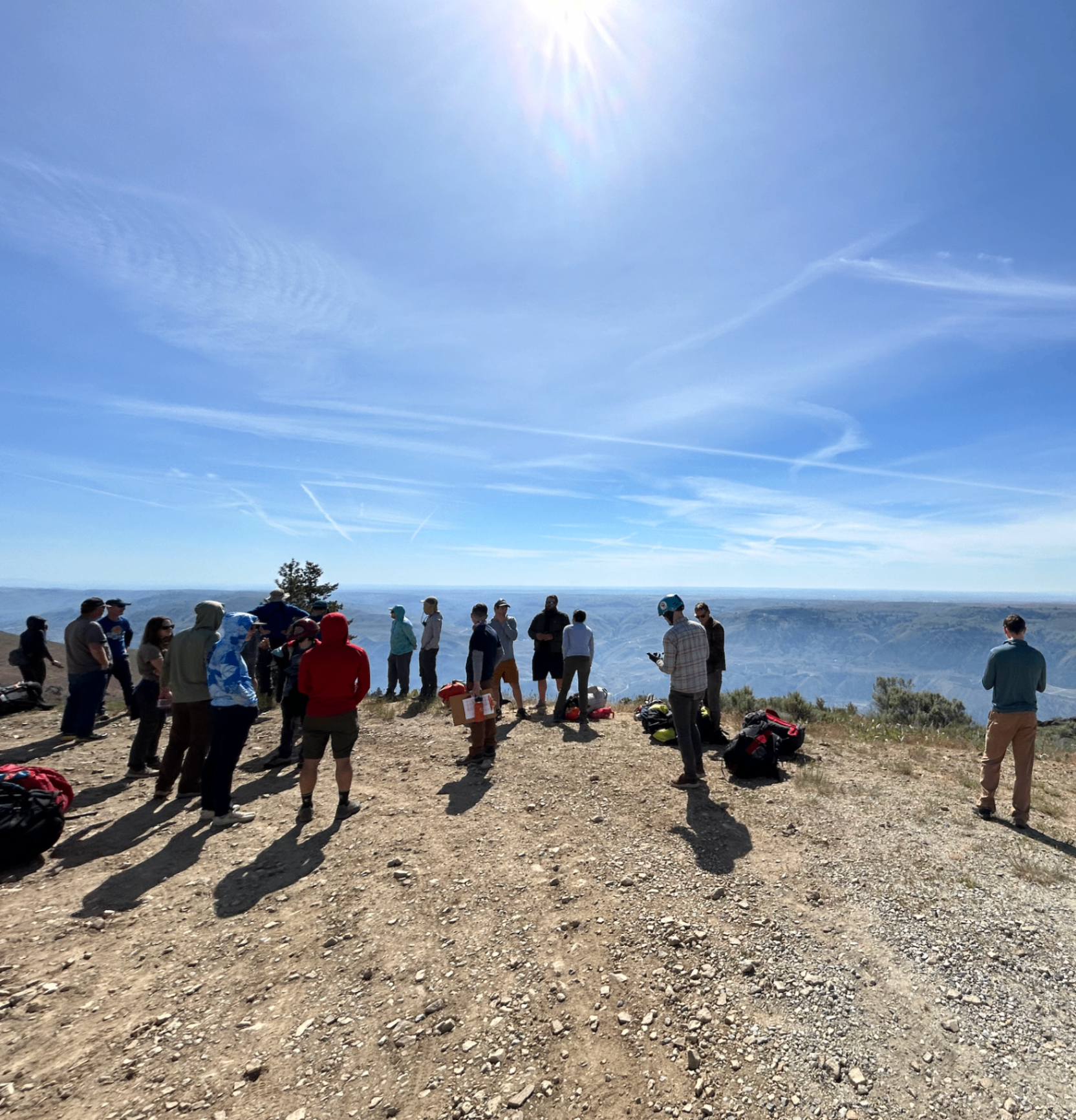 Group standing at cliff edge looking south under bright sun with valley views.