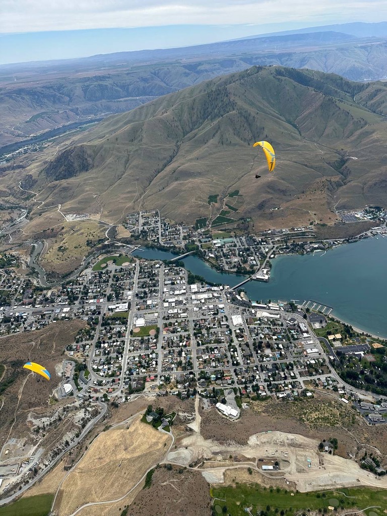 Two paragliders flying over Chelan town and hills