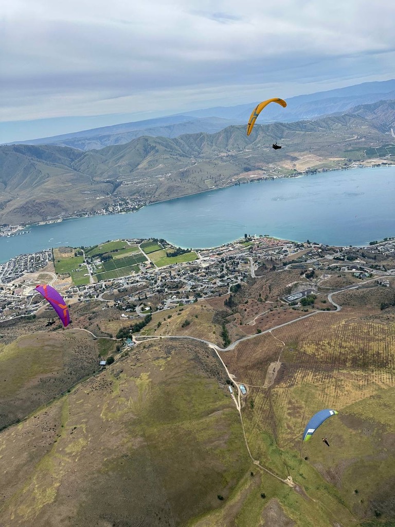 Three paragliders soaring above the hills with Chelan in the background.